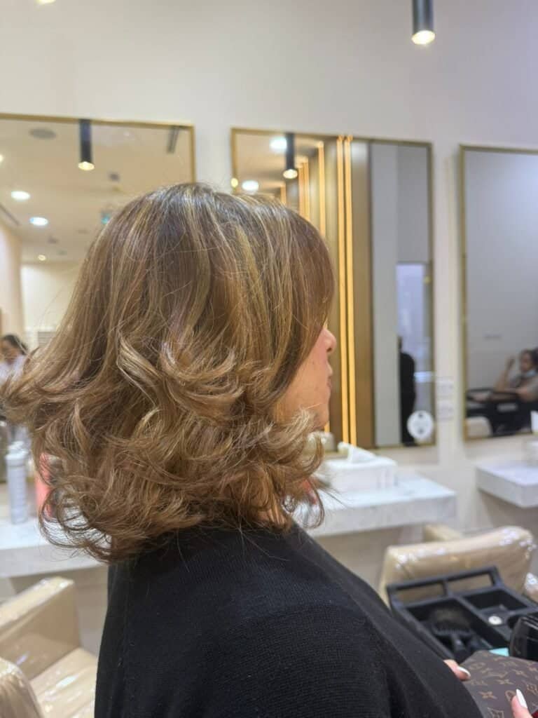 Lush curly hairstyle with caramel highlights at Sasha Beauty Salon Dubai.