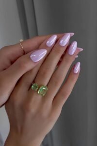 Glossy pastel pink gel nails with gold rings and green gemstone rings, perfect for a stylish manicure.